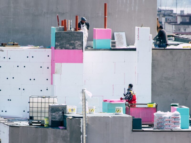 Workers on a city rooftop in bright daylight, engaged in construction activities with colorful insulation materials.